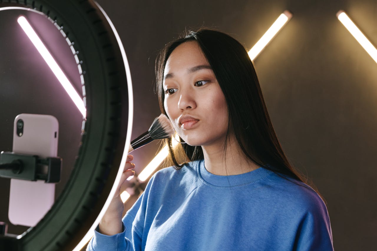 project-03-b Asian woman filming a makeup tutorial for her vlog using a ring light, emphasizing beauty and creativity.