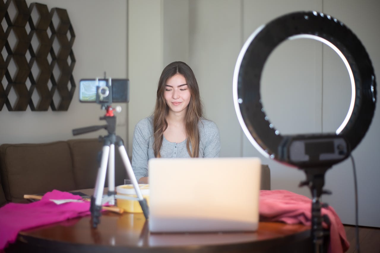 project-03-a A young woman vlogging indoors using a smartphone, tripod, and ring light setup.