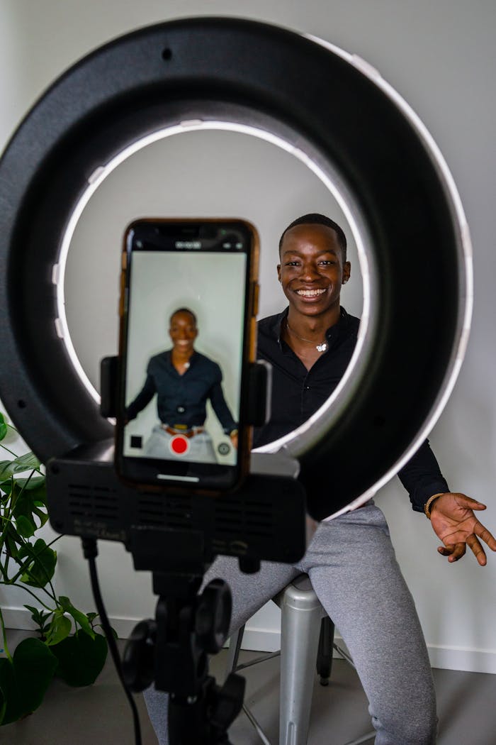 projects-header Smiling African American man recording video indoors using a smartphone and ring light setup.