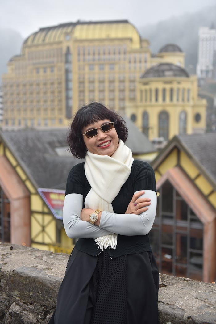 Home Cheerful woman with sunglasses standing before European-style architecture, foggy backdrop.